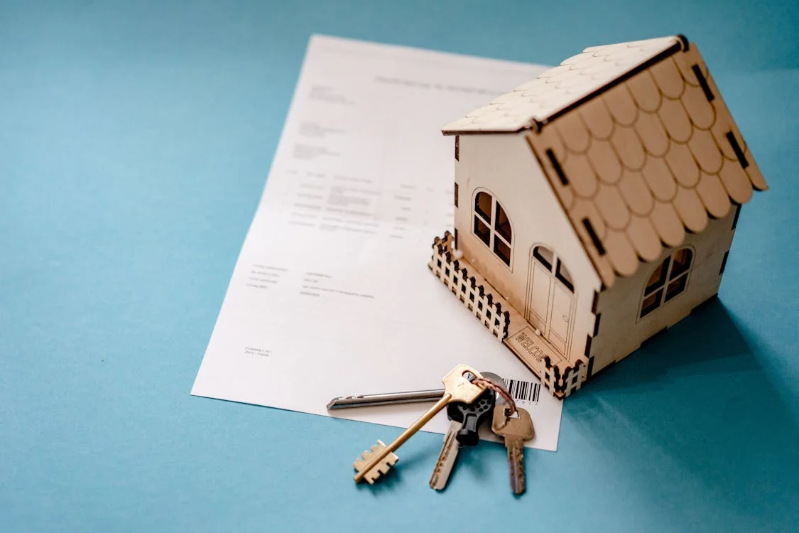 house model, property paperwork, and keys illustrating real estate wealth building through ownership and financing